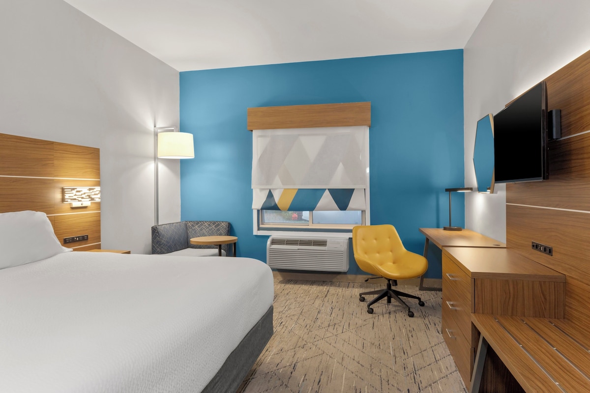 Habitación de hotel con una cama grande, un escritorio, una silla, un televisor y una ventana con persianas.