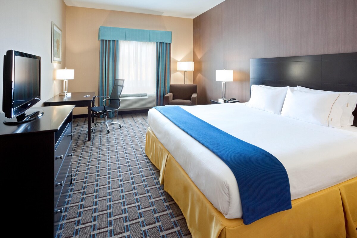 A hotel room with a large bed, a desk with a TV, a chair, and a lamp.