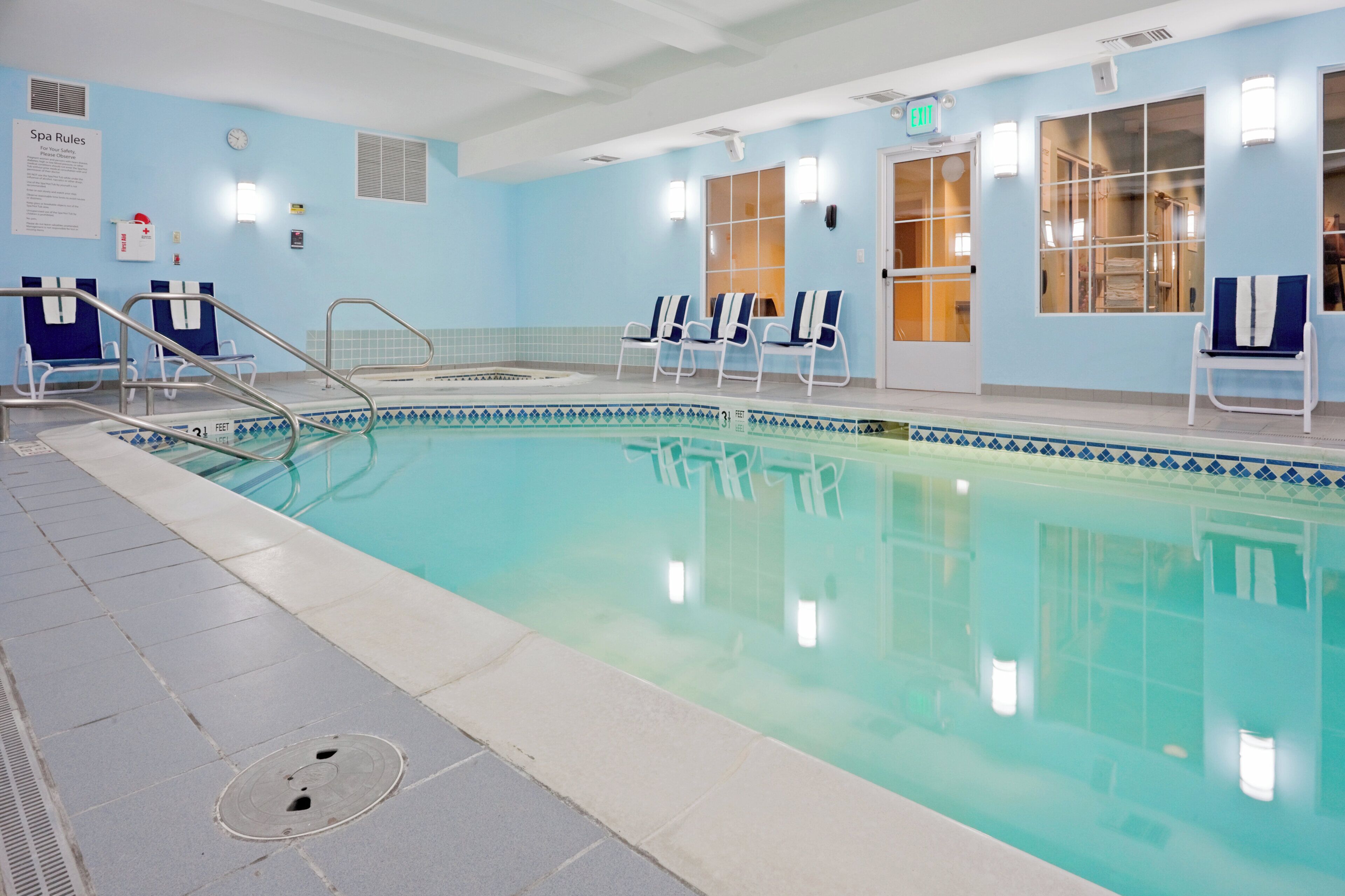 An indoor swimming pool with clear water, a lifeguard chair, and a sign indicating the pool depth.