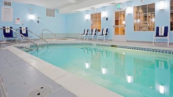 An indoor swimming pool with clear water, a lifeguard chair, and a sign indicating the pool depth.