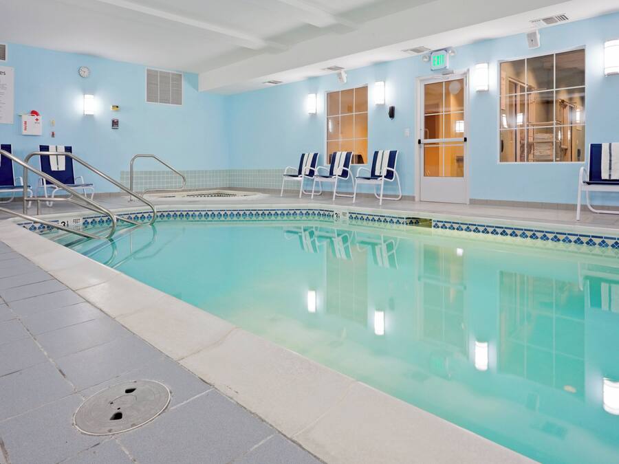 An indoor swimming pool with clear water, a lifeguard chair, and a sign indicating the pool depth.