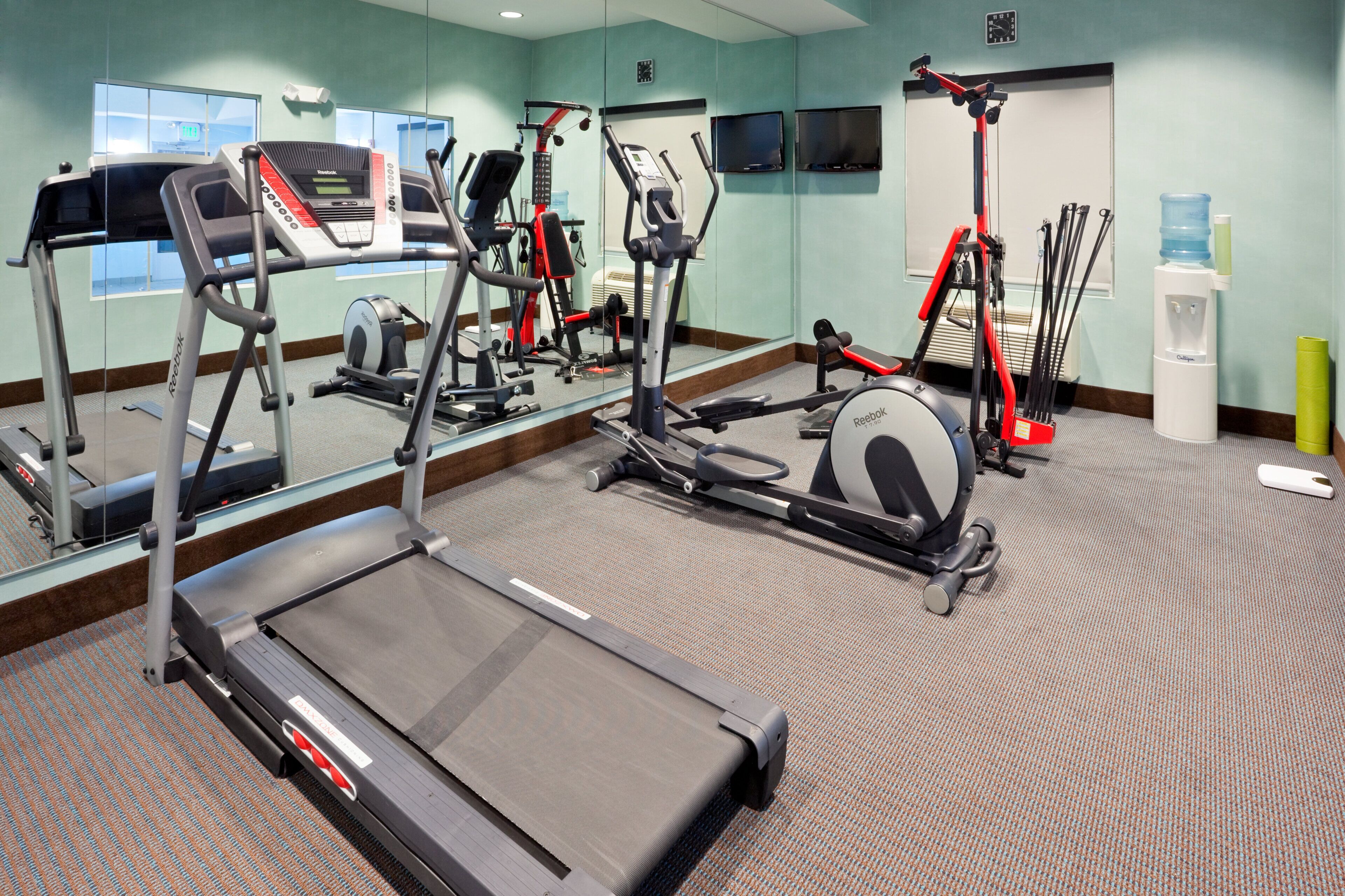 A fitness center with treadmills, elliptical machines, and a water dispenser.