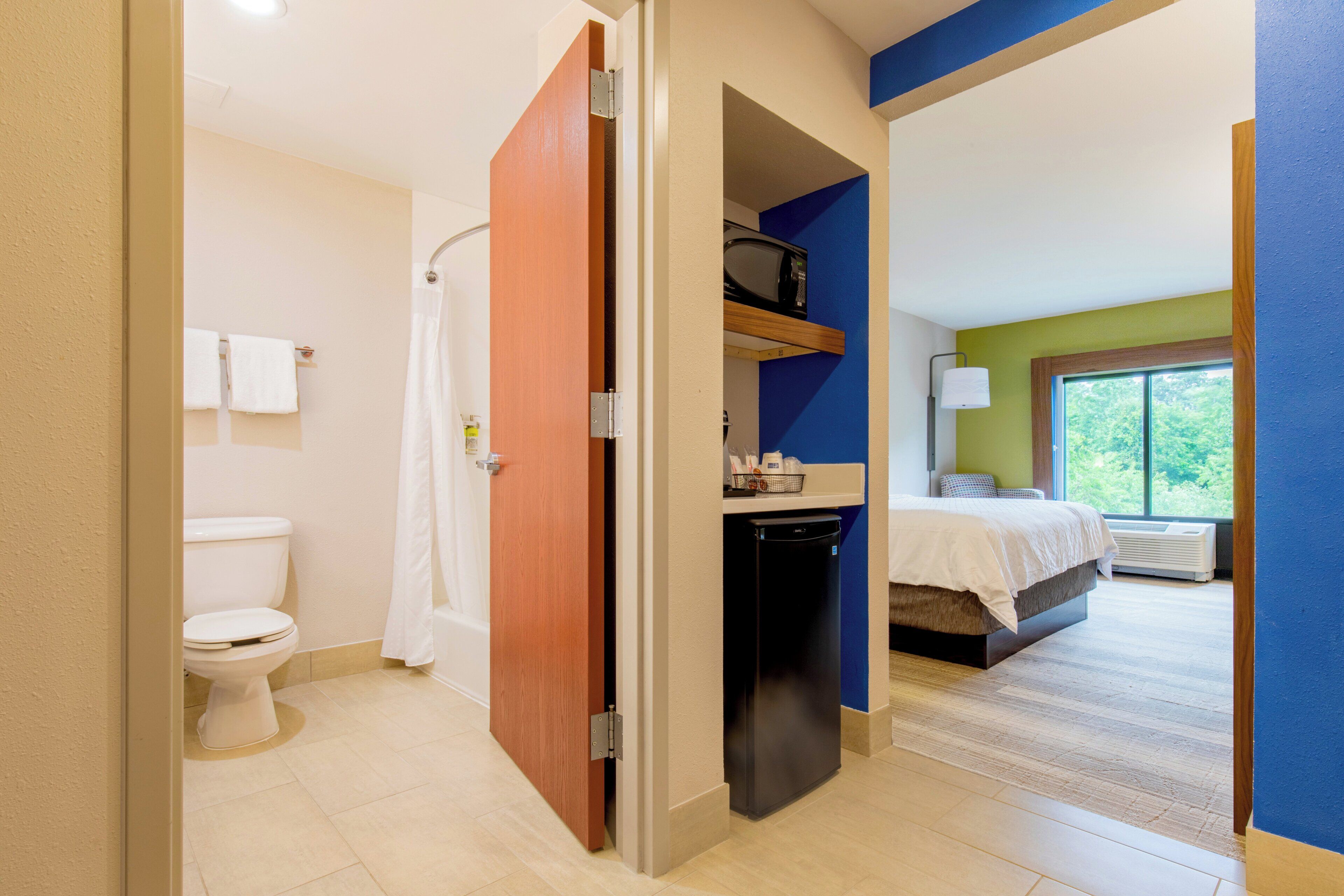 A hotel room with a bathroom, a bed, a microwave, and a window.