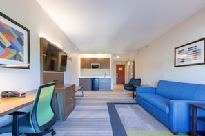 En modern lägenhet med ett litet kök, en matplats, ett vardagsrum med en blå soffa och en arbetsplats med ett skrivbord och en stol.