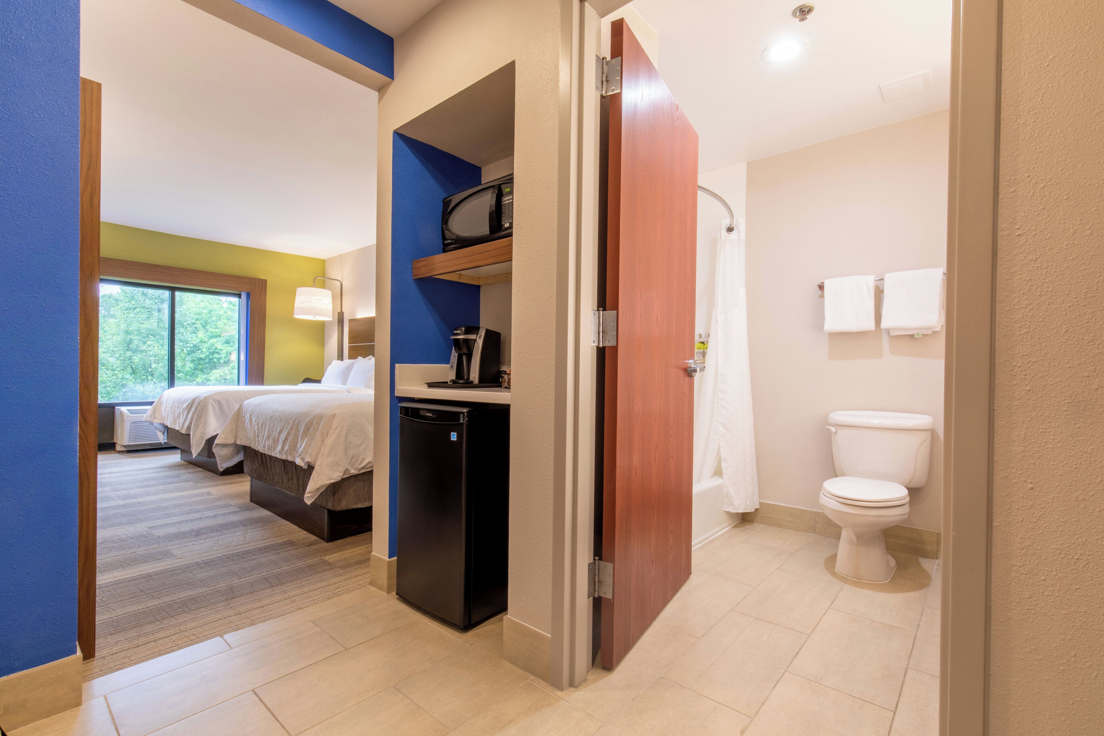 Een hotelkamer met een bed, een kleine kitchenette, een magnetron en een badkamer met toilet en douche.