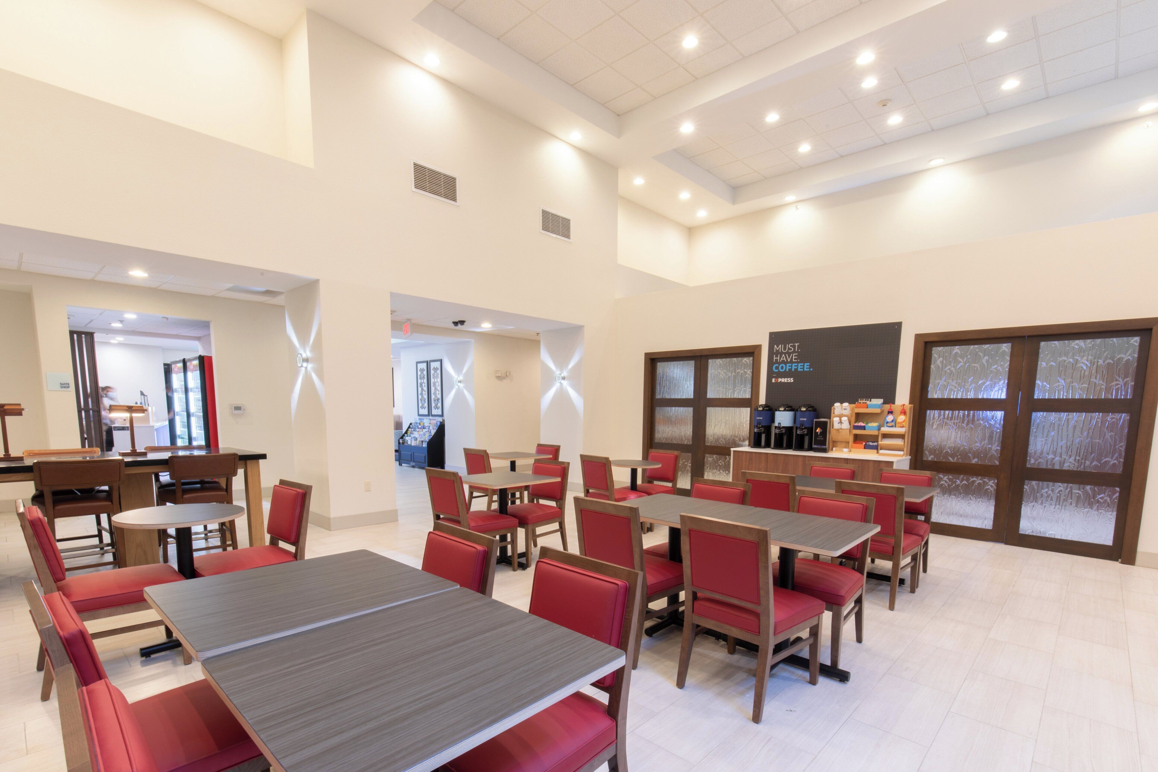 A spacious dining area with multiple tables and chairs, a coffee station, and a view through a patterned glass door.