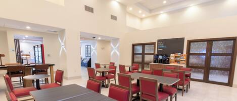A spacious dining area with multiple tables and chairs, a coffee station, and a view through a patterned glass door.