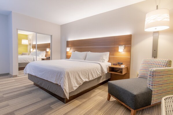 Ett modernt hotellrum med en stor säng, sängbord, en stol och en spegel.