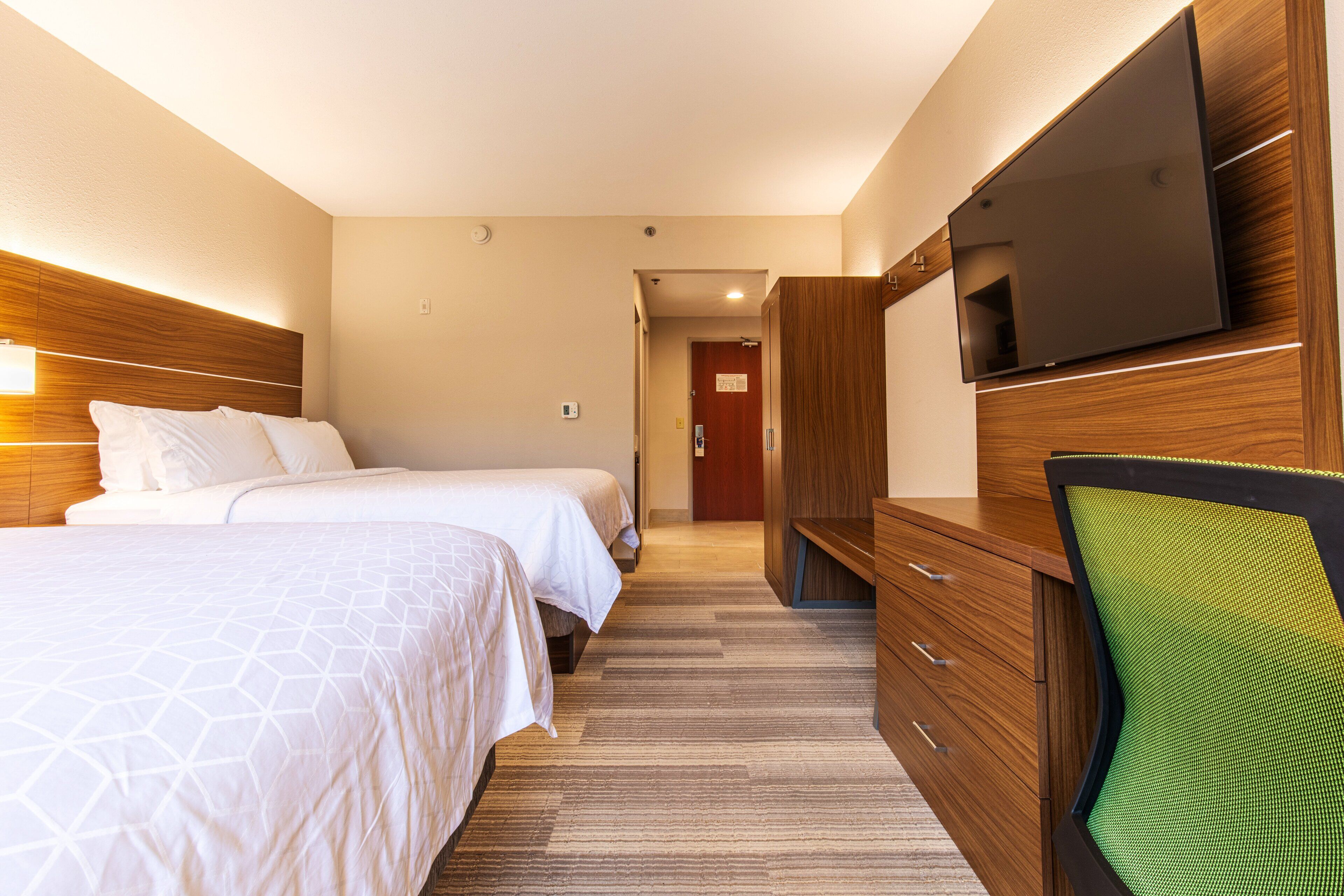 A hotel room with two beds, a TV, a desk with drawers, and a chair.