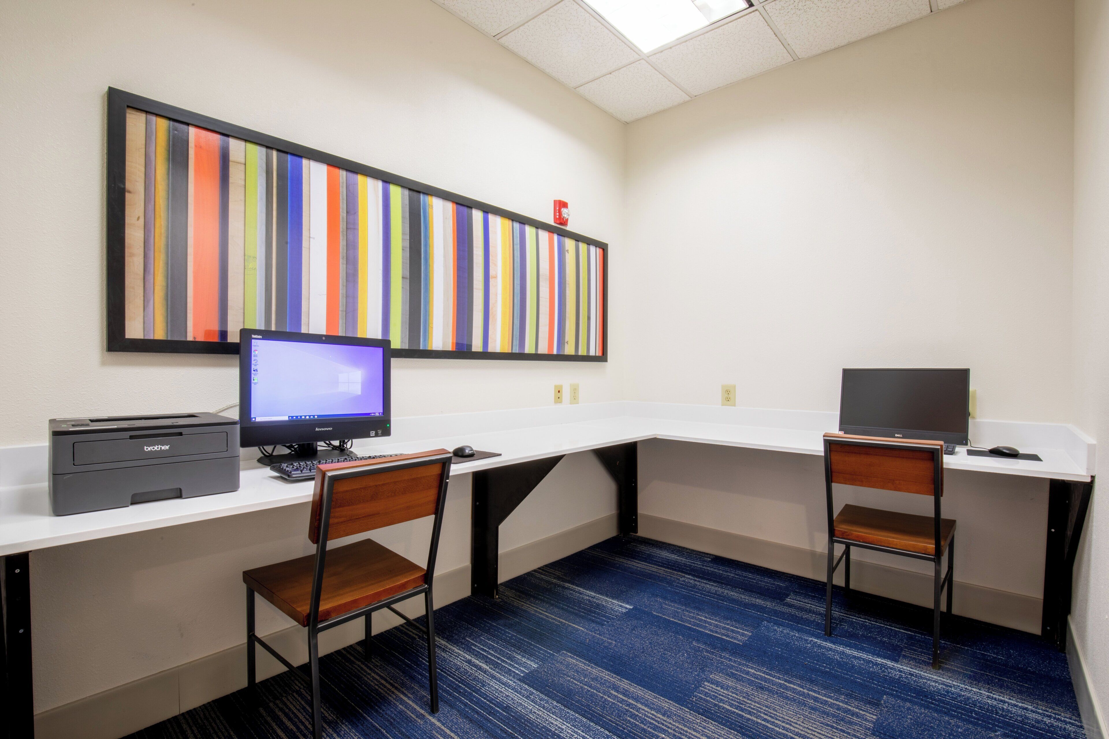 A workspace with two desks, each with a computer and keyboard, a printer, and a chair.
