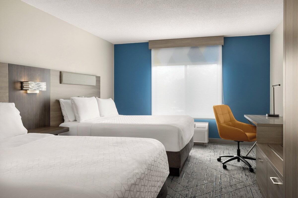 Une chambre d’hôtel avec deux lits, un bureau, une chaise et une grande fenêtre.
