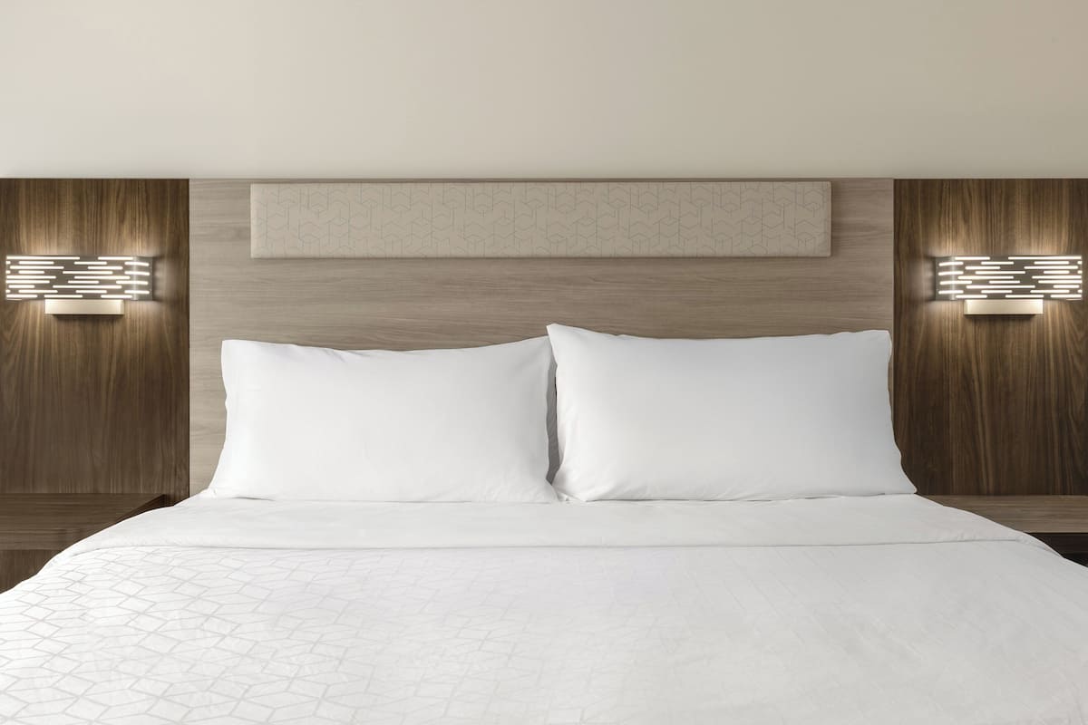 Une chambre d’hôtel avec un grand lit, une tête de lit en bois et deux appliques murales.