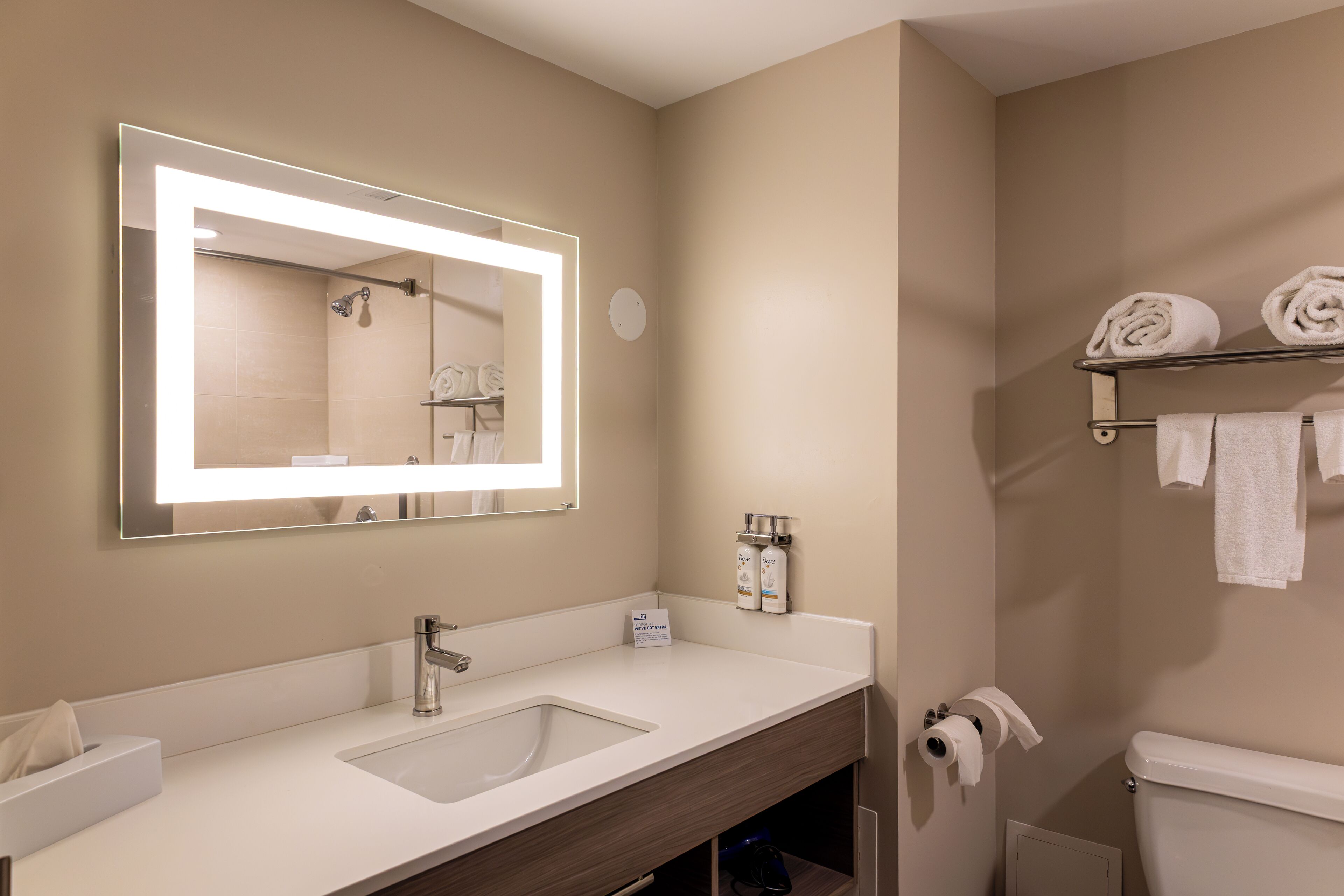 A modern bathroom with a large mirror, a sink, a toilet, and a shelf with towels.