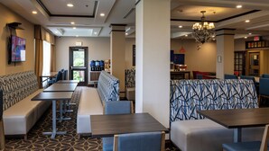 Een hotel lobby met zithoeken, tafels, een kroonluchter en een zichtbaar vluchtroutebord.