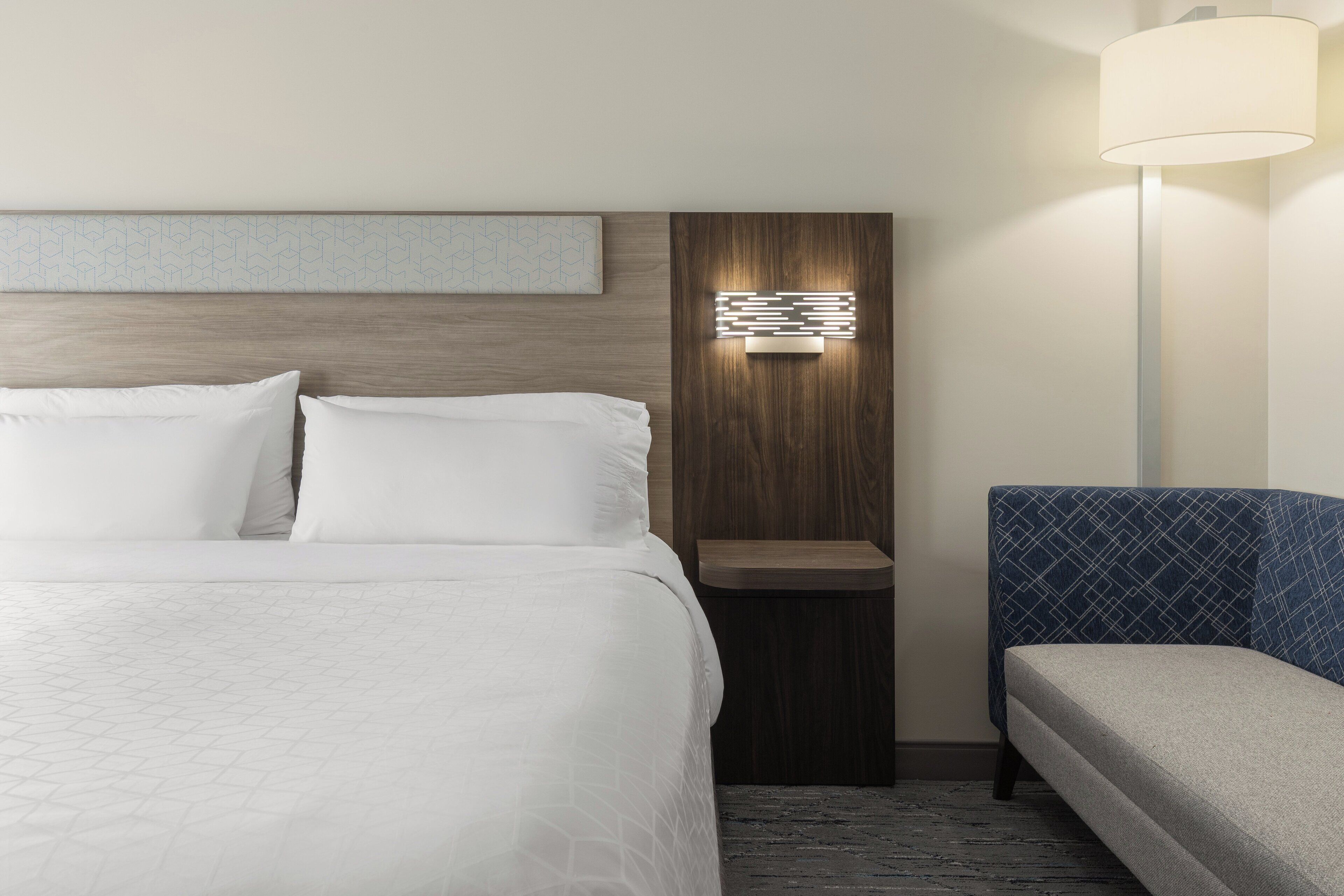 A hotel room with a large bed, a bedside table, a wall-mounted light, and a sofa.