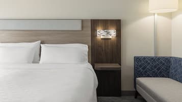 A hotel room with a large bed, a bedside table, a wall-mounted light, and a sofa.