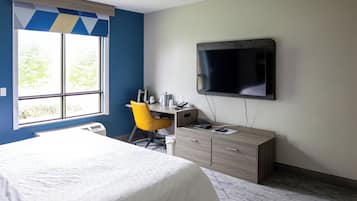 A hotel room with a bed, a desk with a chair, a television, and a window with blinds.