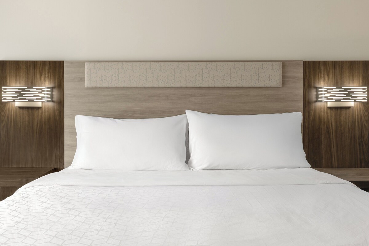 Une chambre d’hôtel avec un grand lit, une tête de lit en bois et deux appliques murales.