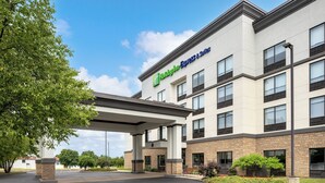 Ein Holiday Inn Express & Suites Gebäude mit modernem Design, das einen überdachten Eingang und eine bepflanzte Fläche mit Bäumen und Sträuchern zeigt.