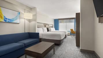 Habitación de hotel con un sofá azul, una mesa de centro de madera, dos camas con ropa blanca, un escritorio con una silla y un cuadro abstracto grande en la pared.