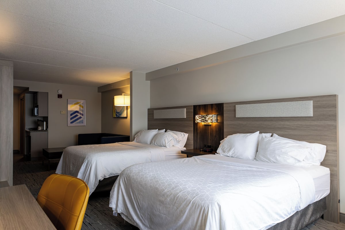 Une chambre d’hôtel avec deux lits, un bureau, une chaise et une petite kitchenette.