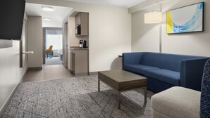 Ein modernes Hotelzimmer mit einem blauen Sofa, einem Holztisch und einem gemusterten Teppich.