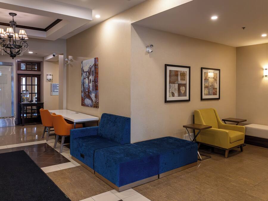 A lobby with a blue sofa, yellow armchair, and a small table. There is a chandelier, framed artwork on the walls, and a sign indicating the location.