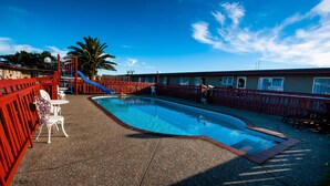 A swimming pool with a red deck, a blue slide, and white chairs. - Charles Court Motel (Greymouth)