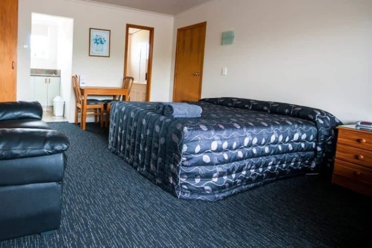 A room with a black leather sofa, a bed with a patterned duvet, a wooden desk, and a chair.