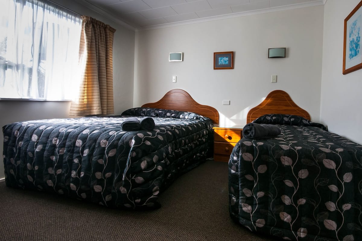 A hotel room with two beds, a wooden headboard, a nightstand, and a window with curtains.