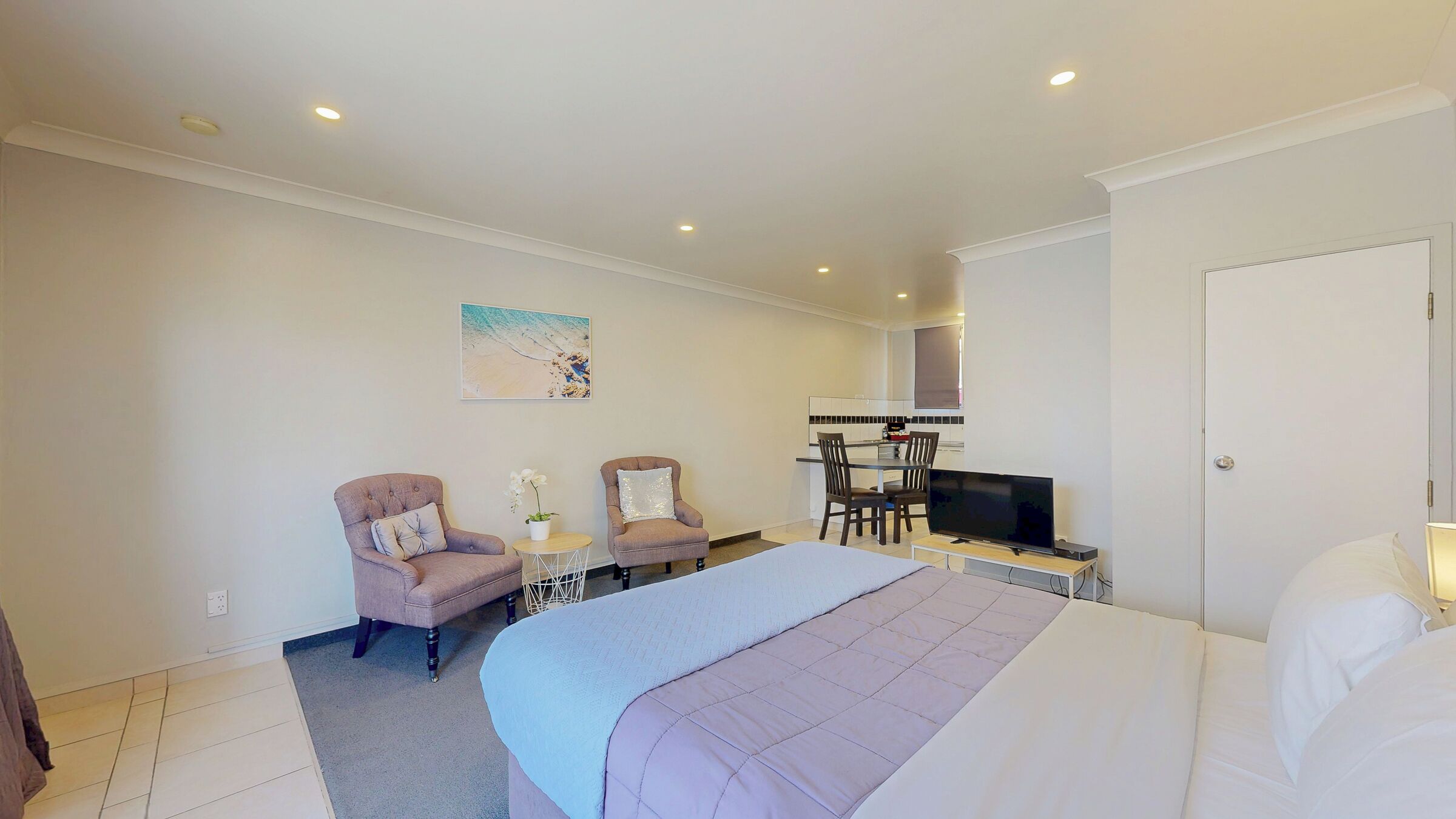 Habitación de hotel con cama, dos sillones, una mesita con una planta, televisión y kitchenette.