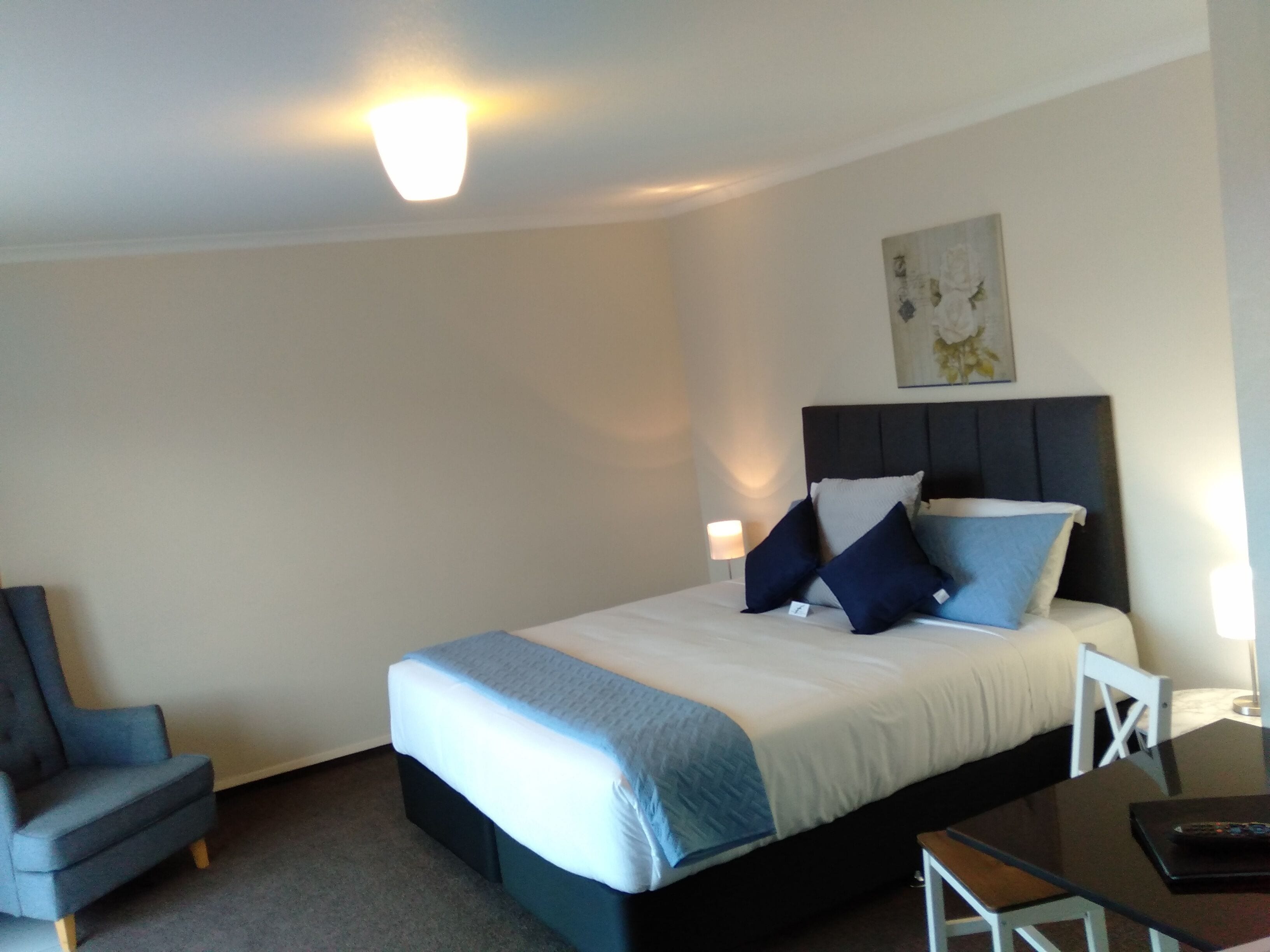 A hotel room with a bed, a chair, a desk, and a lamp.