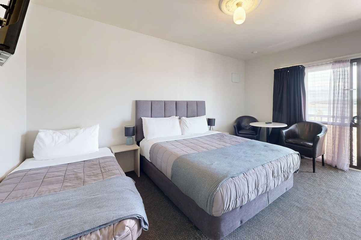 Une chambre d’hôtel avec deux lits, une petite table, une chaise et un balcon avec des rideaux.