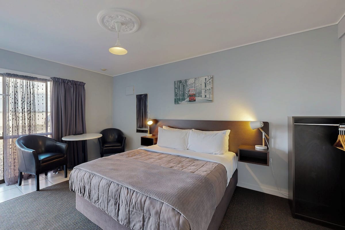 Une chambre d’hôtel avec un grand lit, un bureau, deux chaises, une petite table, une armoire et une vue sur l’extérieur.