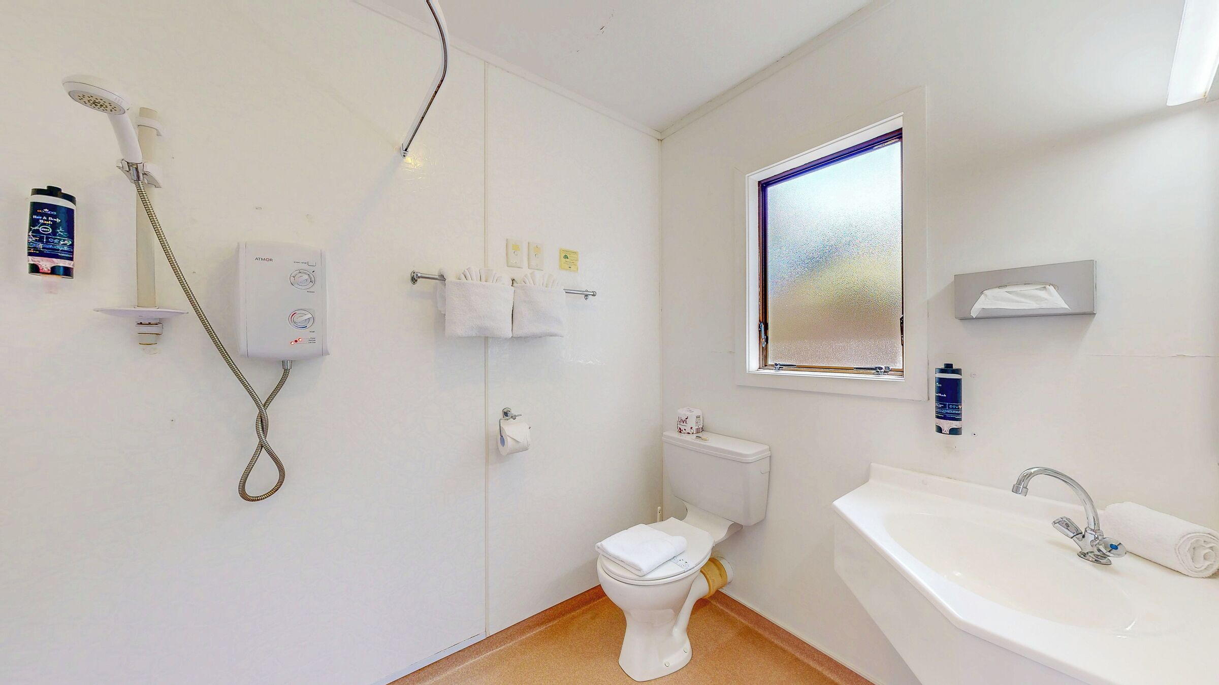 Une petite salle de bain comprenant des toilettes, une douche, un lavabo et une fenêtre.