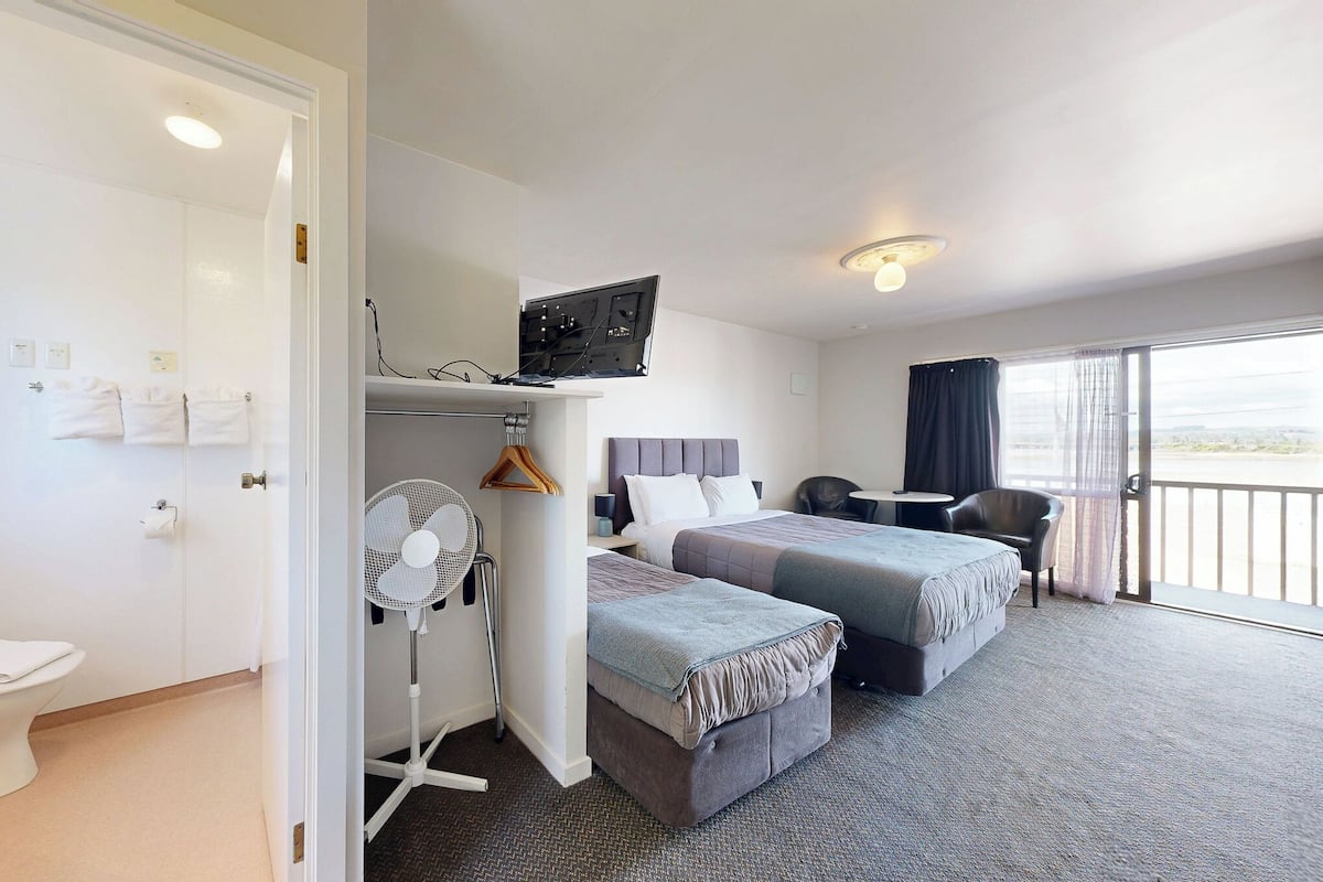 Une chambre d’hôtel avec deux lits, une télévision, un ventilateur et un balcon avec vue.