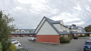 A residential building with a parking lot, featuring a mix of single and double-story houses with pitched roofs. - Homestead Villa Motel (Invercargill)