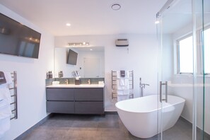 A modern bathroom with a freestanding bathtub, a large mirror, and a flat-screen TV mounted on the wall. - Homestead Villa Motel (Invercargill)