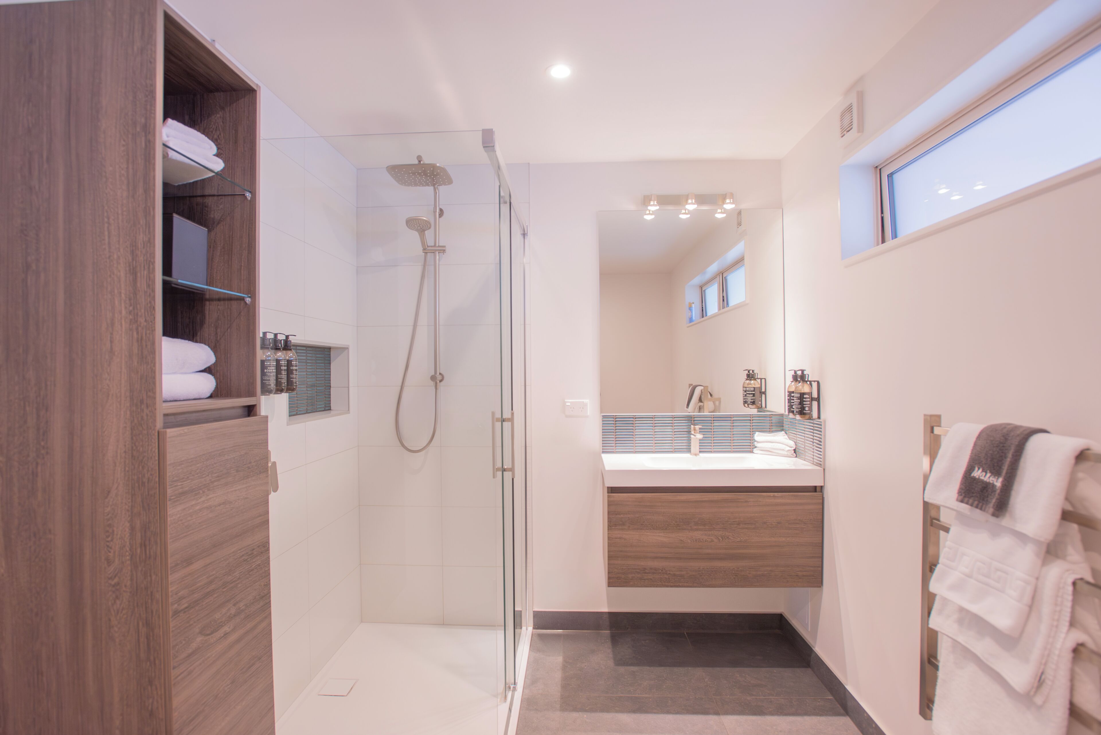 Un baño moderno con ducha envuelta en vidrio, tocador de madera y lavamanos empotrado.