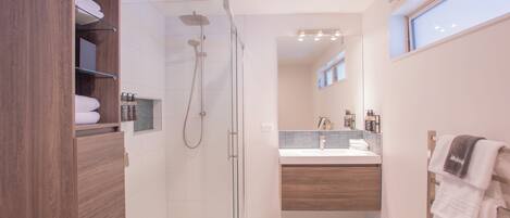 Un baño moderno con ducha envuelta en vidrio, tocador de madera y lavamanos empotrado.