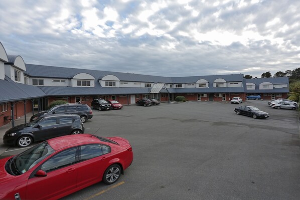 Un parking où plusieurs voitures sont garées devant un bâtiment doté d’un toit bleu et de murs blancs.