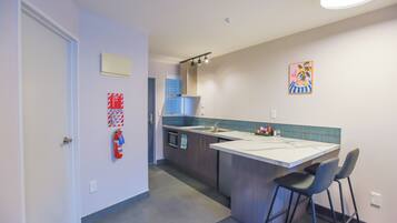 A compact kitchen with a small island, bar stools, a fire extinguisher, and a painting on the wall.