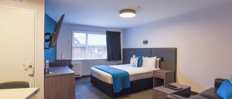 Una habitación de hotel con cama, escritorio, silla y un pequeño sofá.