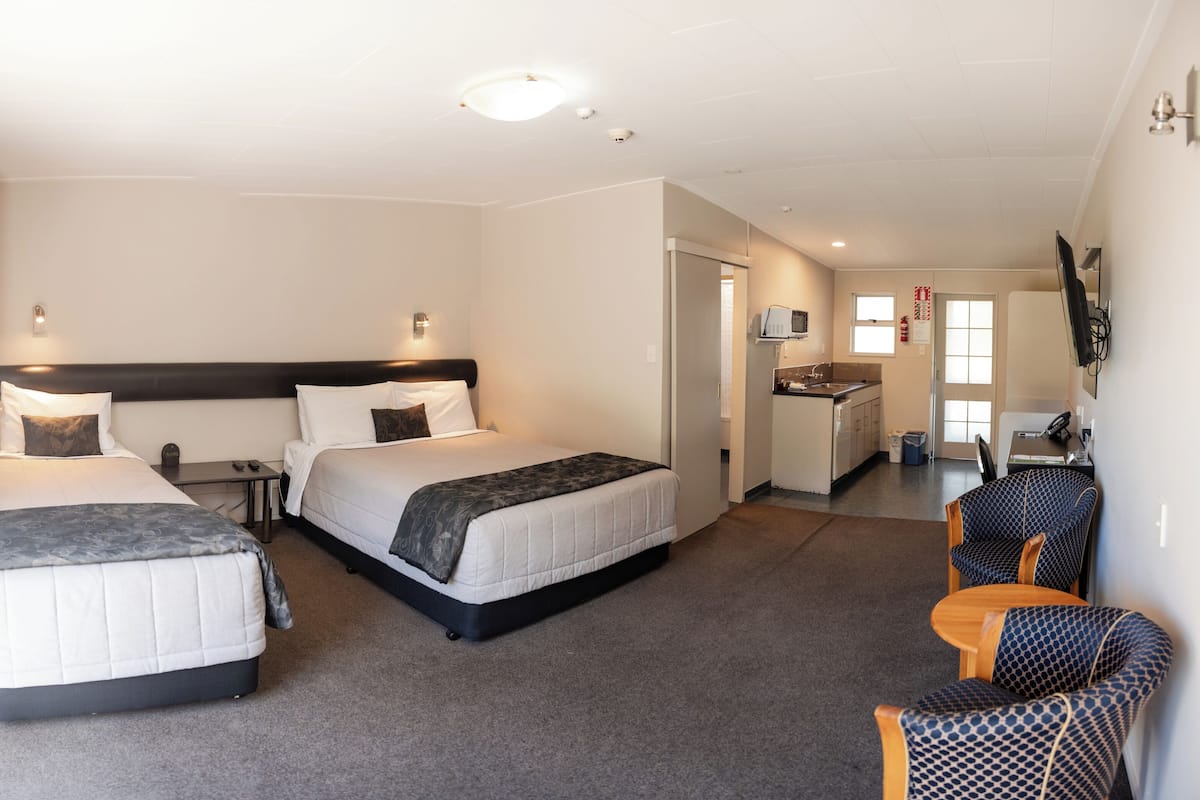 A hotel room with two beds, a desk, a chair, a TV, and a kitchenette.