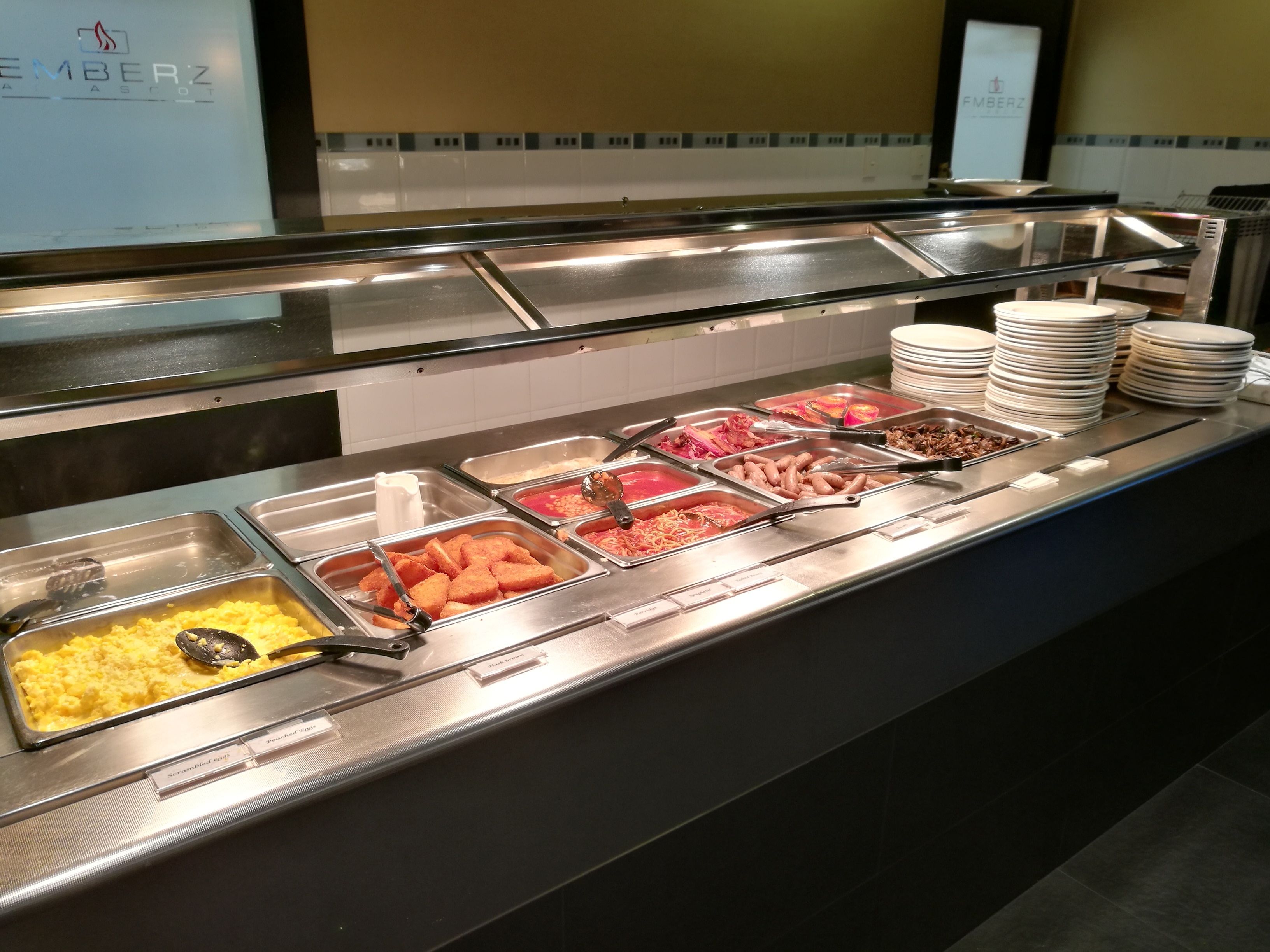 Buffet com diversas opções de comida, incluindo ovos mexidos, salsichas e outros pratos.