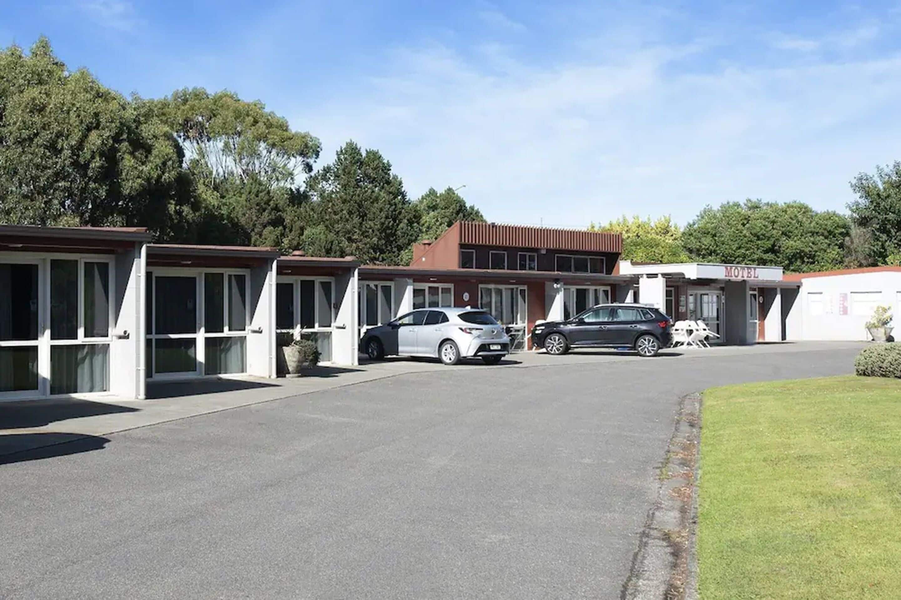 A motel with multiple units, each with a carport. There are two cars parked in front.