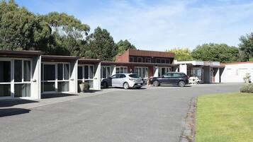 A motel with multiple units, each with a carport. There are two cars parked in front.