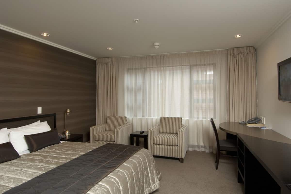 A hotel room with a large bed, two armchairs, a desk, and a chair.