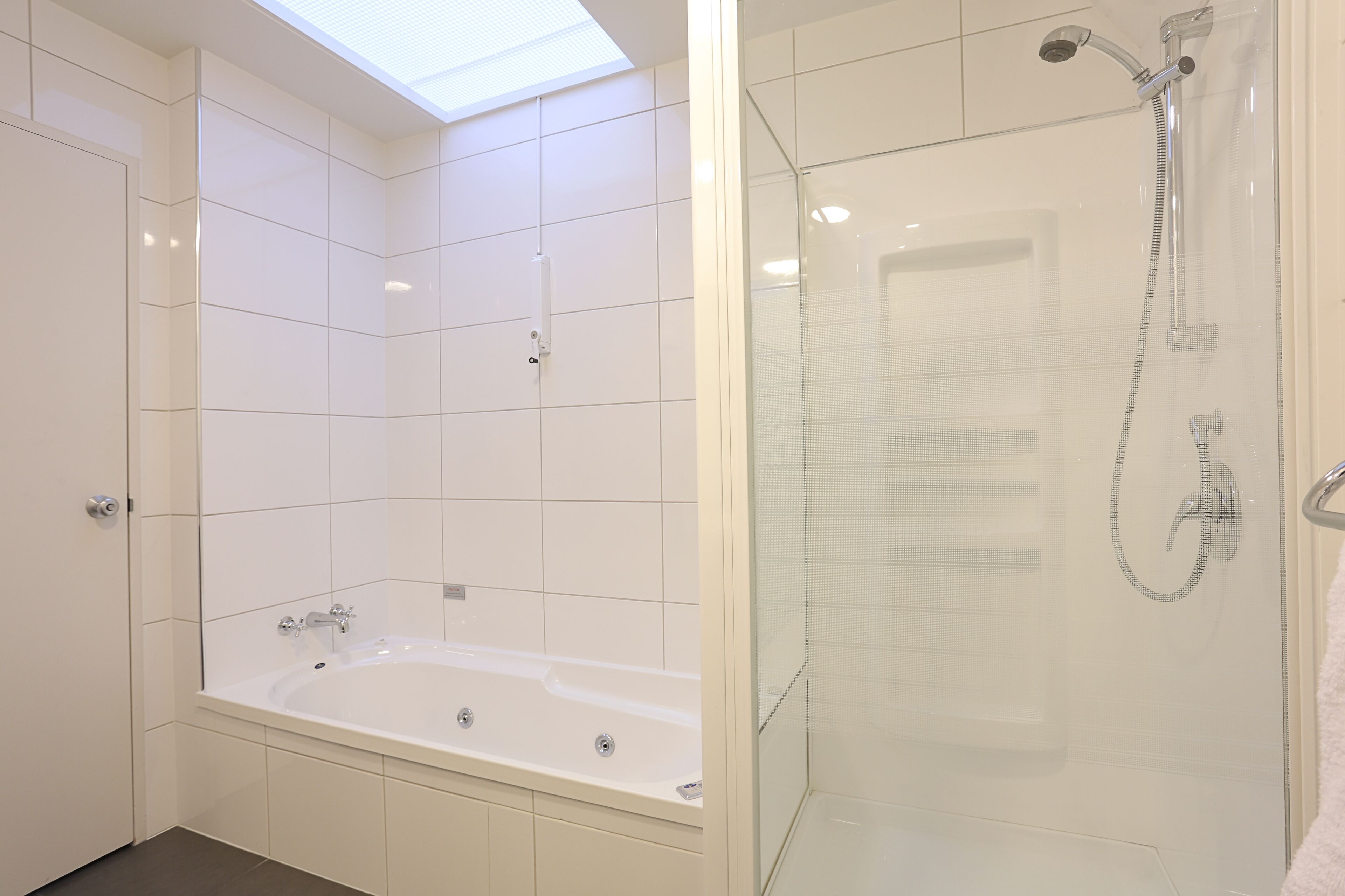 Ein modernes Badezimmer mit einer Glaskabine zur Dusche, einer freistehenden Badewanne und einem Oberlicht über dem Duschbereich.