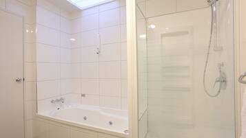 Ein modernes Badezimmer mit einer Glaskabine zur Dusche, einer freistehenden Badewanne und einem Oberlicht über dem Duschbereich.